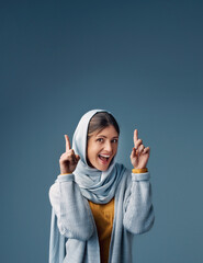 Pointing, woman and hijab in studio, portrait and isolated on blue background. Finger, point and...