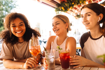 Close-up of three charming girls drinking chilled cocktails in a cafe