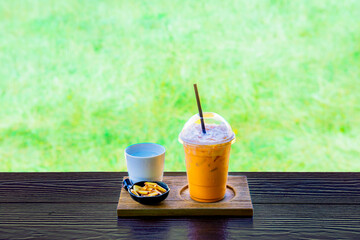 Iced Thai milk tea and cracker in a small bowl with drinking water on a wooden tray