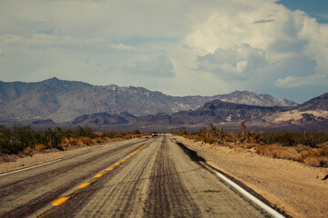 Car driving on a desert road against mountains, with a cloudy sky overhead in the United States