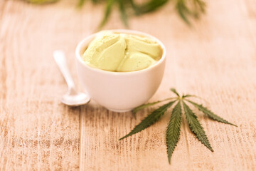 A hemp leaf is lying on a mock-up jars of ice cream on a table