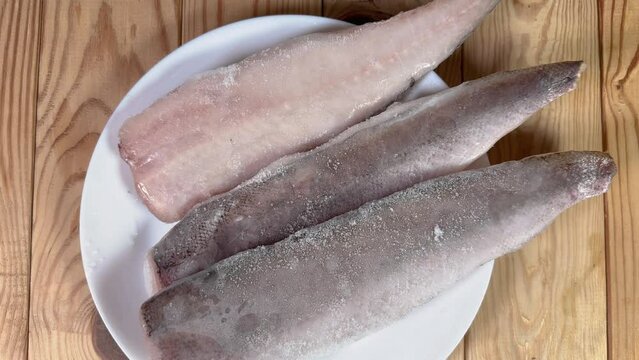 Raw frozen fillets of hake in ice glaze on plate