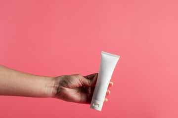 Plastic white tube for cream or lotion. Skin care or sunscreen cosmetic with hand on pink background.