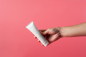 Plastic white tube for cream or lotion. Skin care or sunscreen cosmetic with hand on pink background.