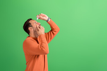 Side view of young man with conjunctivitis putting drops for treatment on isolated green background