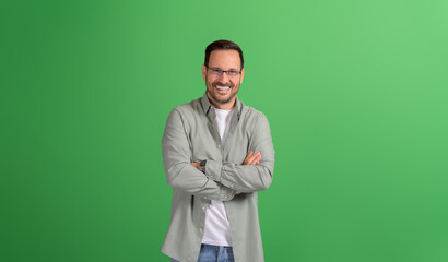 Cheerful young male entrepreneur in eyeglasses and with arms crossed posing over green background