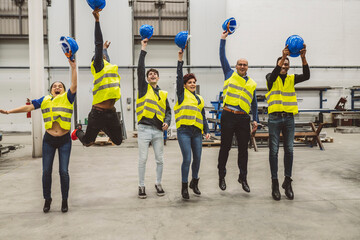 Engineers Celebrating with Jump and Hard Hat Toss in Factory