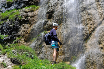 Obraz premium young man in climbing equipment against rock, waterfall, climbs rock, active lifestyle of people, mountaineering, via ferrata in mountains of alps, life insurance in extreme sports
