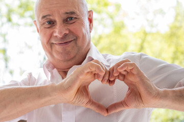 mature charismatic 65-year-old man, Loving senior making heart shape with fingers, Tenderness and...