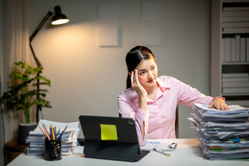 A woman sits at a desk with a stack of papers in front of her