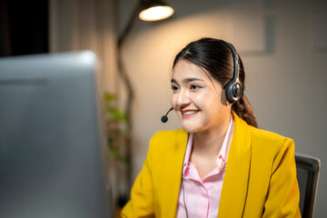 A woman wearing a yellow jacket and pink shirt is smiling at a computer screen