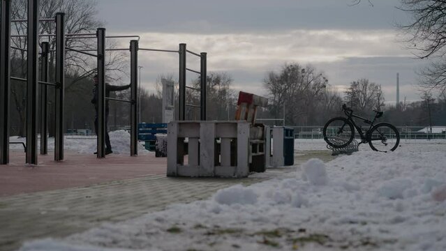 Adult Caucasian man warming up under the metal parallel bars in the park at sunset