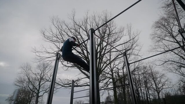 Caucasian man doing gymnastic moves on the metal parallel bars near to leafless trees in the park
