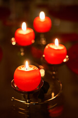 Closeup of four red candles illuminated in the dark, resting on a mirrored tray atop a black surface