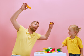 Building memories together. Father and his little son construct toy with colorful building kit against pink studio background. Concept of Happy Father's day, family holidays celebration, parenthood.