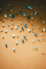 Origami paper cranes on wall against orange background.