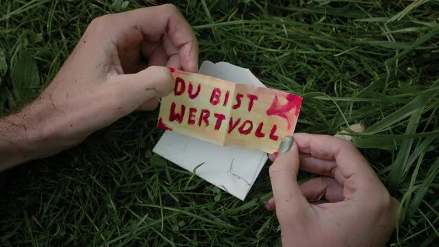 Adult male hands opening a fold paper with German text "Du Bist Wertvoll" means "You are valuable"