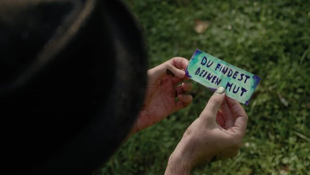 Closeup footage of adult male hands opening a fold paper with German text "Du Findest Deinen Mut"