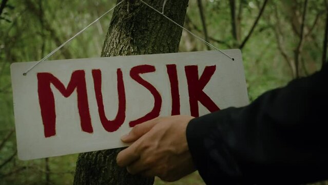 Slow motion closeup shot of male hand touching a white sign with word" MUSIK" hanging on tree trunk