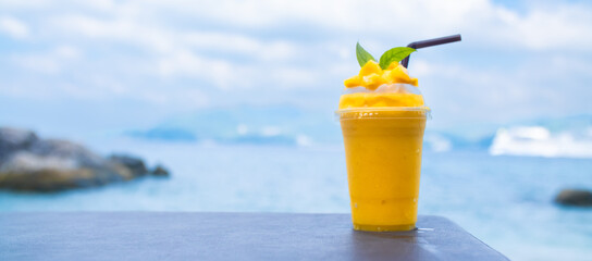 Smoothie made from fresh mango fruits against the backdrop of a seascape. Fruit and yoghurt ice...