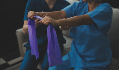 Personal trainer assisting senior woman with resistance band. Rehabilitation physiotherapy worker helping old patient at nursing home. Old woman with stretch band being coached by physiotherapist.