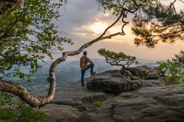  man in a checkered shirt enjoys the early morning mountain landscape.He stands on the top, put his...