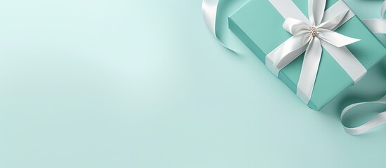 Copy space image of a top view flat lay featuring a white gift box adorned with a tiffany satin ribbon against a serene mint blue backdrop