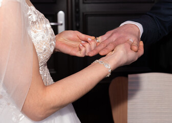 Cropped view of bride and groom, bride putting wedding ring on groom's finger 