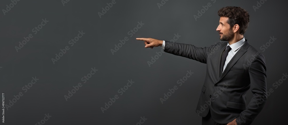 Poster A professional man in a suit is seen sideways with his finger pointing upwards against a grey background creating an image with enough empty space for additional content or ideas