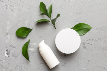 Organic cosmetic products with green leaves on cement background. Flat lay