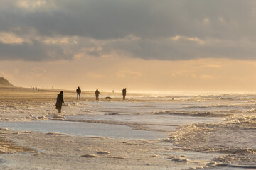 Group of people enjoying an evening stroll along the beach, illuminated by a beautiful sunset