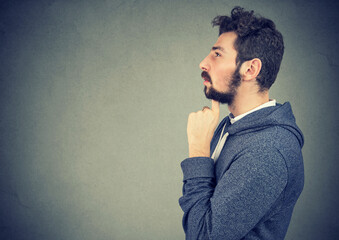 Side profile of a man standing with hand on chin thinking about question with pensive face...