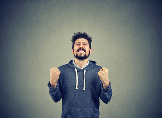 Cheerful young man celebrating success with fists pumped  isolated grey wall background