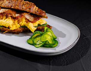 Delicious croissant sandwich with scrambled eggs, bacon, and avocado on a plate