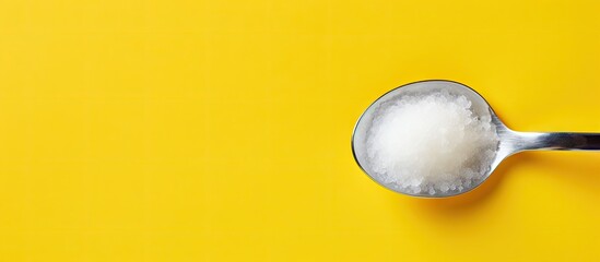 Yellow background with a spoon containing sea salt Copy space available for text