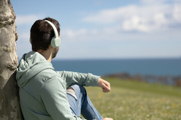 Man in the park listening to music with his green headphones. Happy man dancing listening to music with his wireless headphones. Man outdoors on a viewpoint with the sea in the background. Copy space.