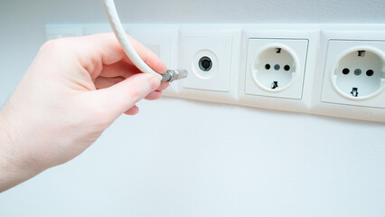 Inserts the antenna cable to the TV outlet. A man inserts a coaxial cable plug into a TV antenna...