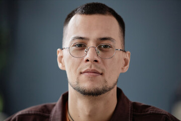 Obraz premium Minimal close up portrait of adult Asian man wearing glasses and looking at camera against grey wall indoors copy space