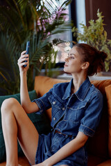 Young woman sitting on a comfortable sofa with a smartphone in hand, deeply focused on the screen