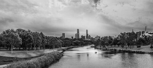 Grayscale of a river flowing through a modern city with skyscrapers on a cloudy day