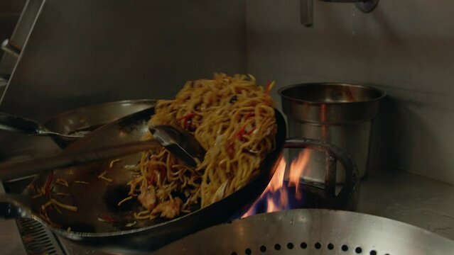 Closeup of hands of a chef stirring pasta in a pan with big spoon at Lok Mela Festival in Pakistan