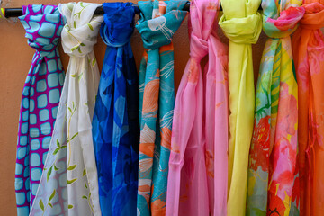 Variety of vibrant, multicolored scarves hanging on an orange wall