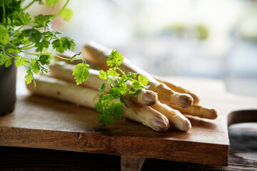 Fresh white asparagus and parsley on wooden cutting board. Seasonal spring vegetables with parsley....
