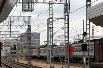 Industrial landscape with contact network at a railway junction and moving passenger train out of railroad station on cloudy day