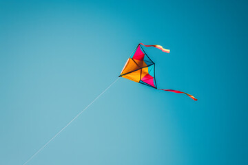 A vibrant photo of a colorful kite flying on a solid blue sky background
