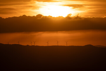 Silhouette of wind turbines on the  mountain range under the dramatic sky at sunset