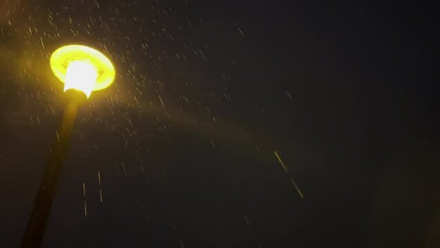 Illuminated old style streetlight on lamppost glowing in the rain at night.

