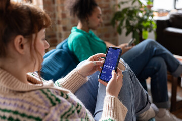 Over the shoulder view of young woman with friend checking financial data with mobile banking app on a smartphone