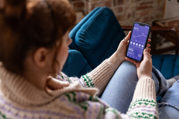 Over the shoulder view of young woman checking financial data with mobile banking app on a smartphone