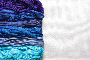Threads of different shades of blue on white fabric. 
